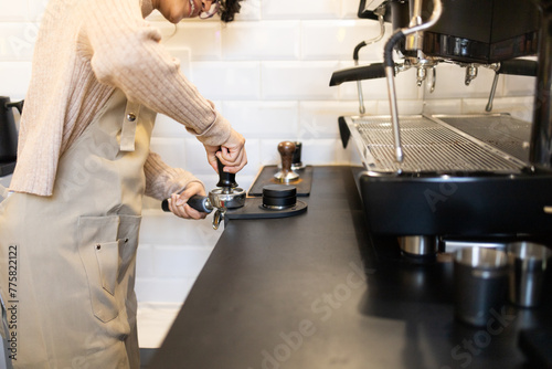 Hispanic woman barista tamping coffee at espresso machine photo