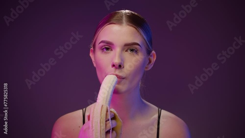 Sexy woman eats a piece of a banana, concept oral sex, purple studio light