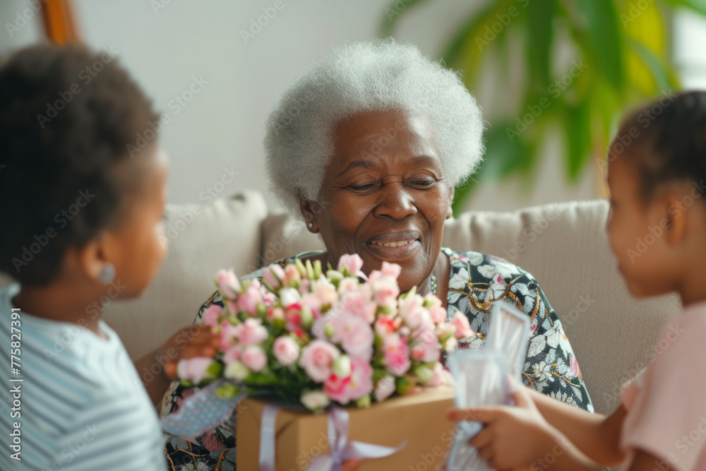 Happy senior African American woman receives presents from her grandchildren. Children make their grandmother a birthday surprise. Little kids give their grandma a gift card and a bouquet of flowers