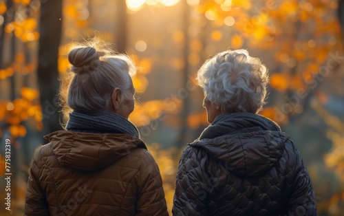 Two women are walking in the woods, one wearing a brown jacket and the other wearing a black jacket