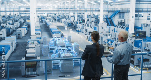 Male and Female Standing at Electronics Factory, Using Computer and Having a Conversation. Augmented Reality Visualization of a Conveyor Belt Production Line with Robot Arms Appears In Front of Them