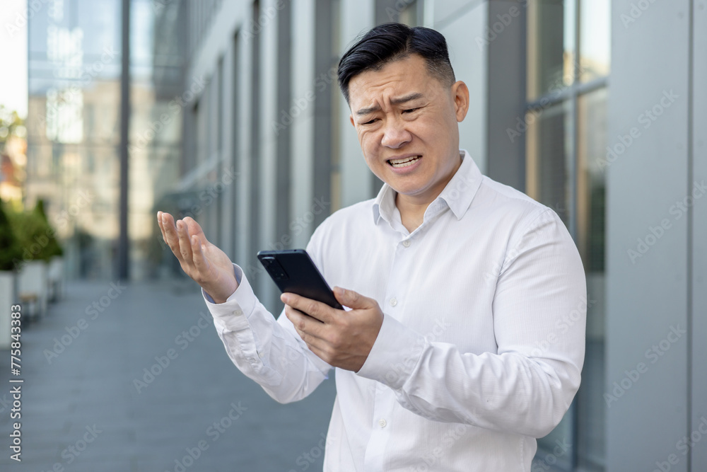 Angry and worried young Asian male businessman standing outside a