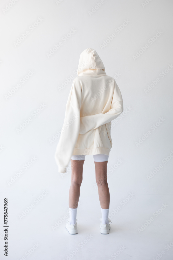Beautiful blonde woman posing in white hoodie and leggings posing against white background. Posing with his back.