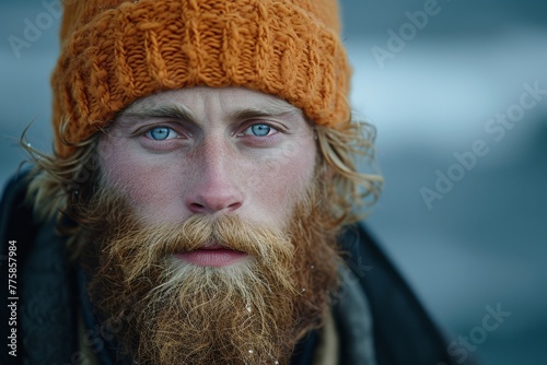 Portrait of a bearded man with long hair wearing an orange knitted hat looking into the camera