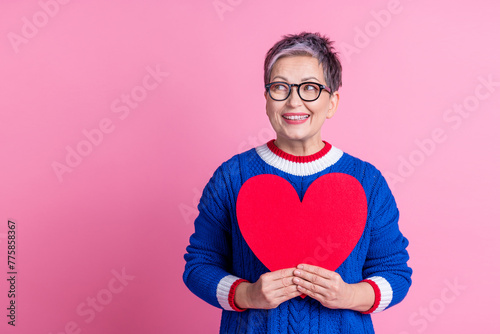 Photo of pretty lovely retired woman wear stylish clothes hold red paper card heart shape empty space isolated on pink color background © deagreez