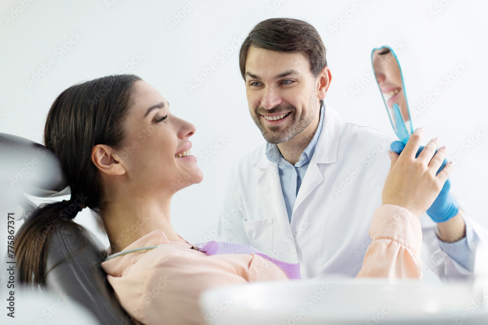 Happy woman patient looking at mirror at her perfect teeth treatment result during dental check up in dentist cabinet, side view Happy woman patient looking at mirror at her perfect teeth treatment result during dental check up in dentist cabinet, side view