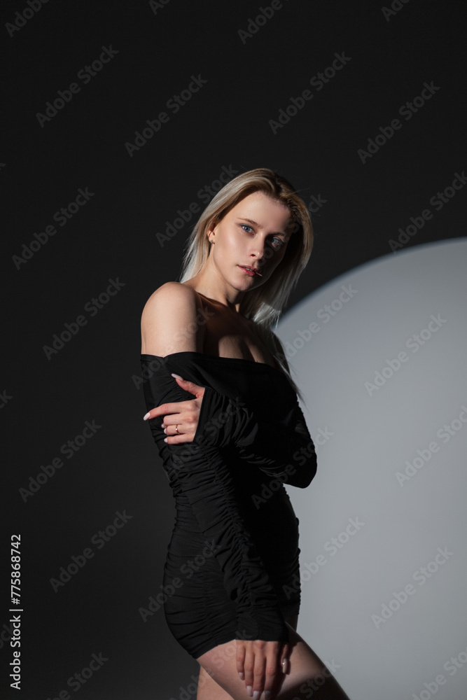 Beautiful fashion sensual girl in a black sexy dress stands and poses in the studio on a dark background Beautiful fashion sensual girl in a black sexy dress stands and poses in the studio on a dark background