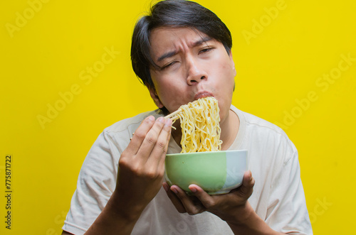 A young Asian man is devouring noodles with his hungry expression turning into one of deep satisfaction.