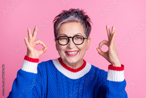 Photo of nice aged lady demonstrate okey symbol wear blue sweater isolated on pink color background photo