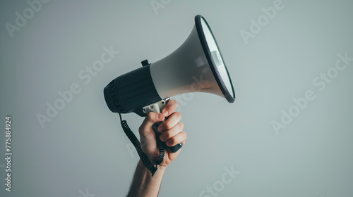 A minimalistic image showing a lone hand holding a sleek black megaphone against a gray background