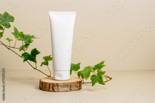 Mockup unbranded cream tube on wooden podium with branch of green leaves. Skincare beauty product container template for design. Natural organic skincare, facial serum, body lotion, face cream