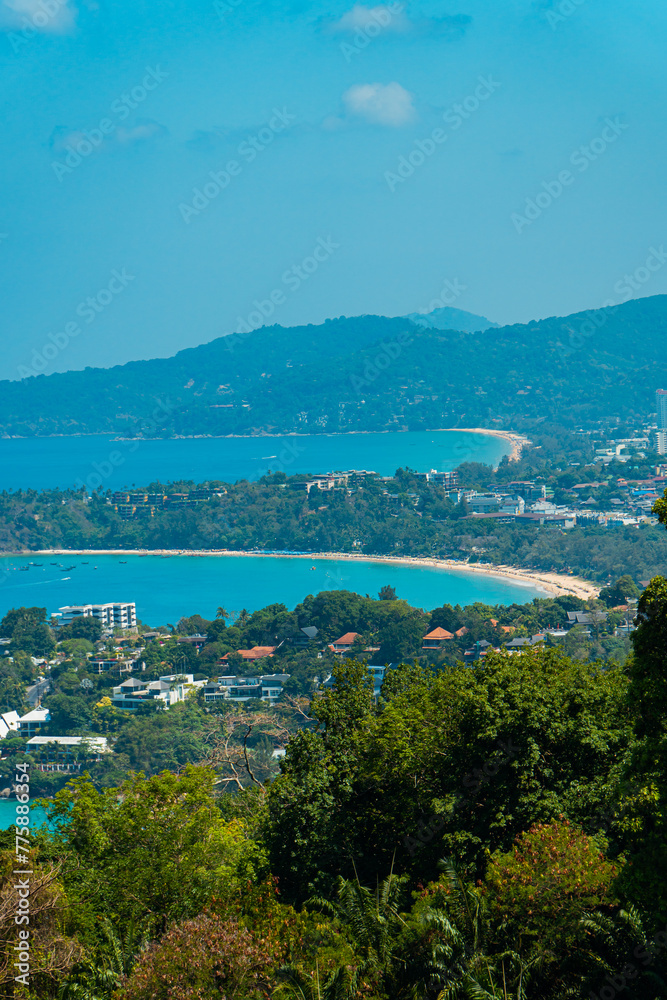 Viewpoint of Karon Beach, Kata Beach and Kata Noi in Phuket, Thailand. The beautiful coastal basin and surrounding buildings are visible from a distance and the sky is blue from a high vantage point.