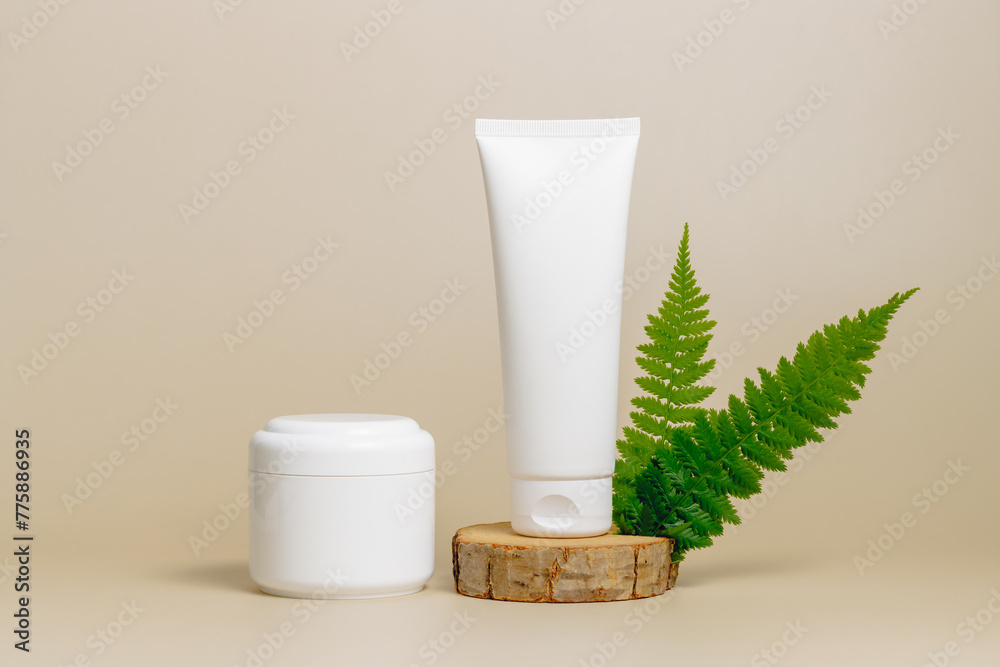 Mockup unbranded cream set containers on wooden podium with green fern leaves. Skincare beauty products, cream tube and bottle template for design. Natural organic skincare, facial cream, body lotion