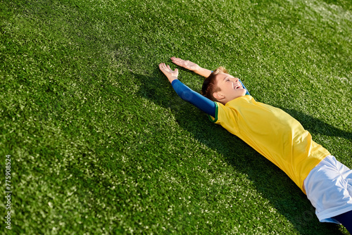 A young boy in a soccer uniform lies peacefully on the grass, staring at the sky with a smile on his face, lost in thoughts of the beautiful game.