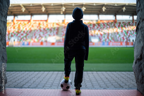 Young the boy with the ball standing in the players' tunnel and looking at the stadium photo