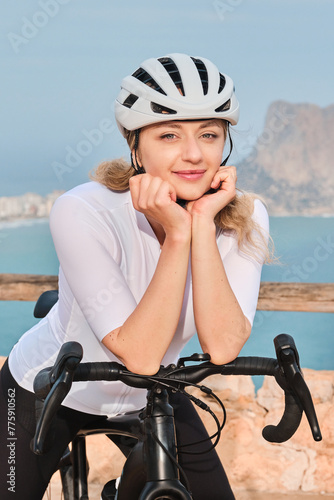 Close up portrait of a female cyclist on sea background. Beautiful woman cyclist is wearing cycling kit, sunglasses and helmet. Sport equipment.Training outdoors. Calp, Alicante, Spain