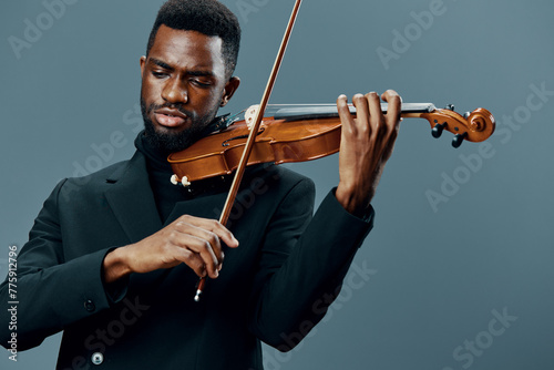 Elegant African American man in black suit playing violin on gray background in musical performance