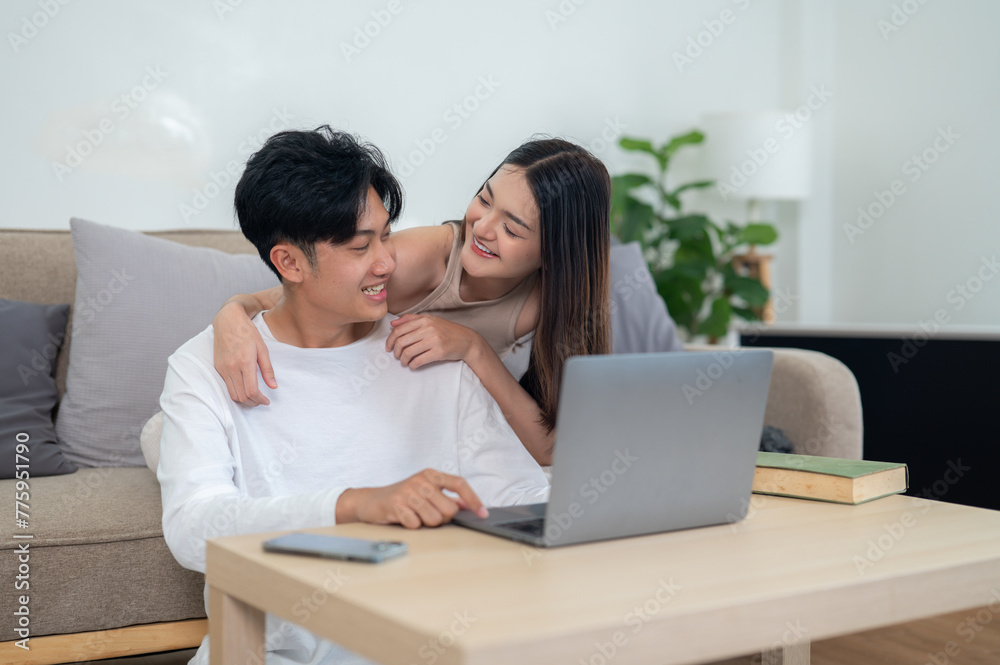 An Asian couple smiling and engaging with a laptop screen while sitting on a sofa in a cozy living room environment.