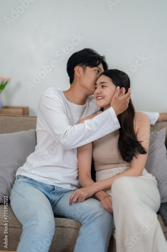 Cute Asian couple hugging and kissing couple's foreheads on the sofa. Sharing smiles and warm hugs in the comfort of their living room.