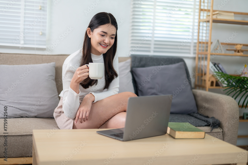 A young woman enjoys a leisurely day, comfortably using her laptop while reclining on a couch at home. A young woman enjoys a leisurely day, comfortably using her laptop while reclining on a couch at home.