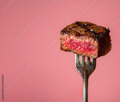 Food concept. A bite size perfectly raw mid cooked steak fillet on fork on pink background, close up	