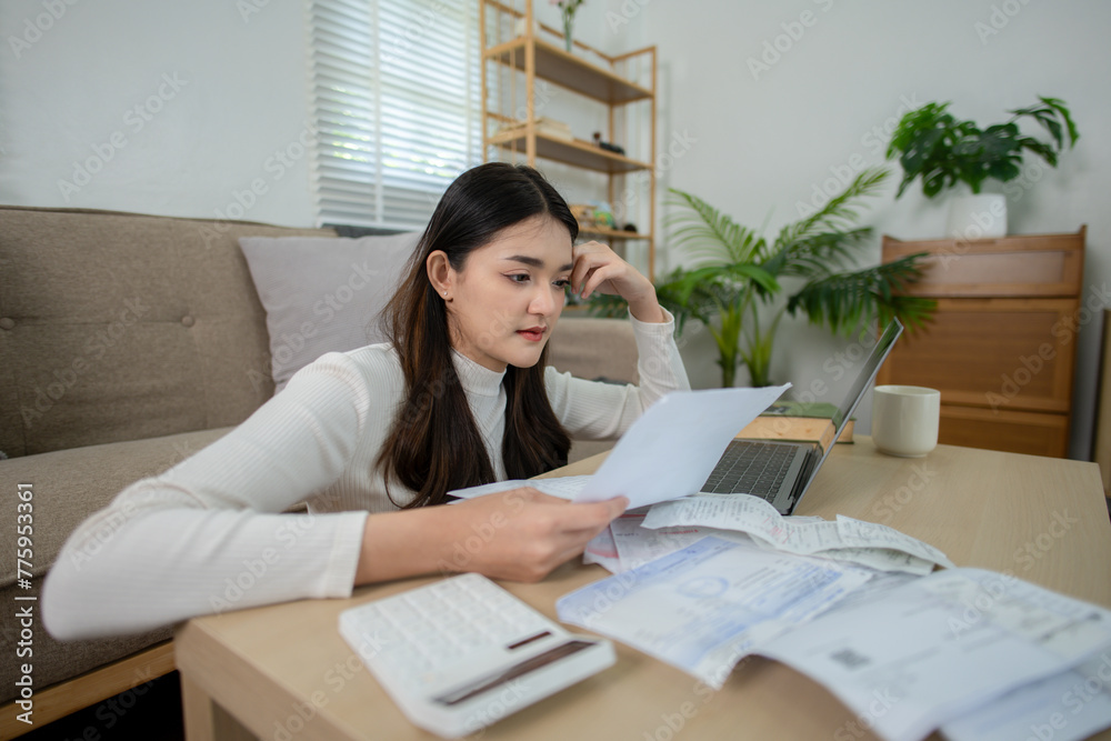 A worried young woman examines financial documents with a hand to her forehead, suggesting stress, with a laptop open in front of her at home. A worried young woman examines financial documents with a hand to her forehead, suggesting stress, with a laptop open in front of her at home.
