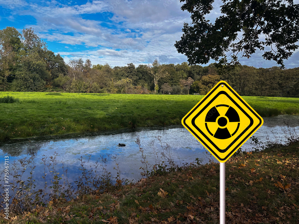 Radioactive pollution. Yellow warning sign with hazard symbol near river outdoors