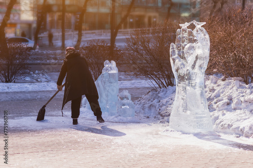 A man uses a shovel to shovel shards of ice next to ice sculptures at the city's winter festival of master sculptors. Sunlight on the figure of hands with birds