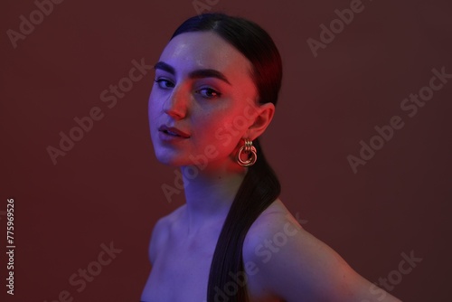 Portrait of beautiful young woman on color background in neon lights