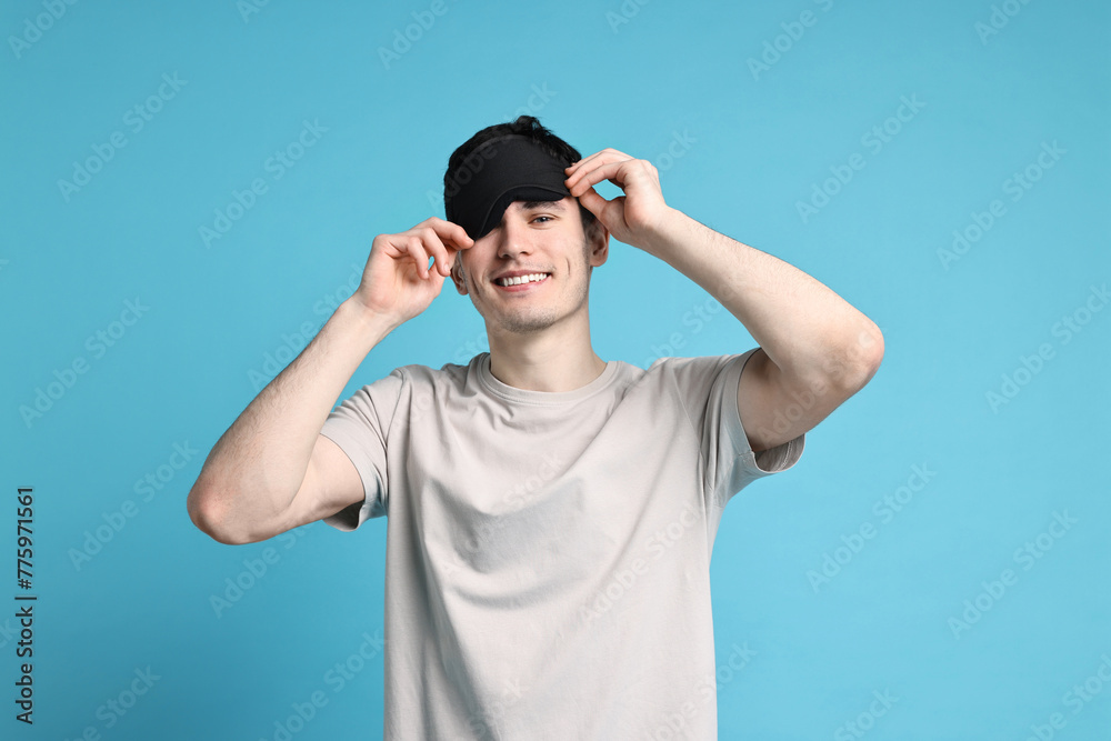 Naklejka premium Happy man in pyjama and sleep mask on light blue background