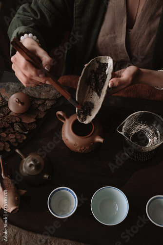 A tea master is transferring loose leaf tea from a clay dish into a traditional Chinese teapot. The image is taken from a top angle. The concept of a Chinese tea ceremony. vertical
