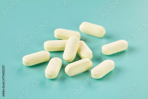 Pile of medicine in the form of mini caplets scattered on a cyan background