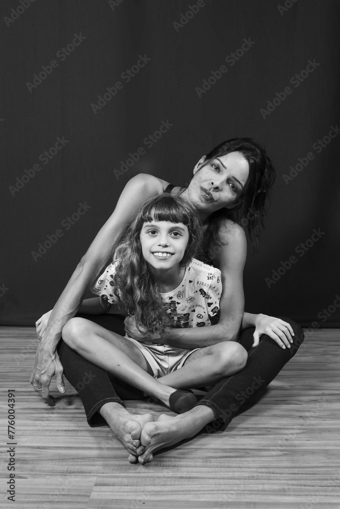 Portrait of Caucasian mother and daughter sitting on wooden floor against dark green background Portrait of Caucasian mother and daughter sitting on wooden floor against dark green background