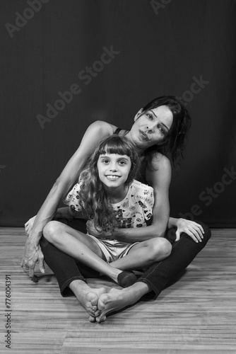 Portrait of Caucasian mother and daughter sitting on wooden floor against dark green background