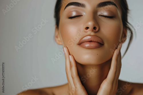 Young woman with closed eyes touching her neck, isolated on a grey background. Beauty and skin care concept. 