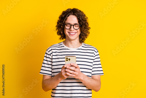 Photo portrait of handsome teenager guy hold device chatting friend dressed stylish striped garment isolated on yellow color background