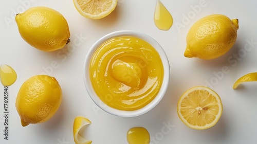 Fresh lemon curd in a white bowl surrounded by whole lemons on a white surface, top view