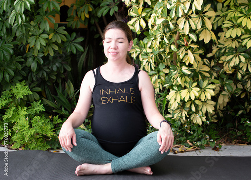 Pregnant woman practicing yoga outdoors. Maternity yoga with tropical background. 