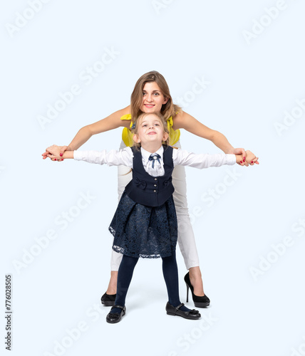 A happy young mother with her little daughter in school clothes, isolated on a light blue background