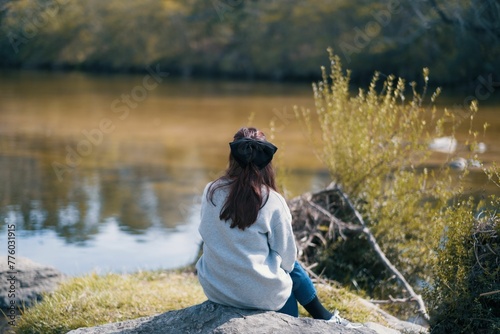 Scenic view of a woman sitting on a rock by the riverbed on a sunny day photo