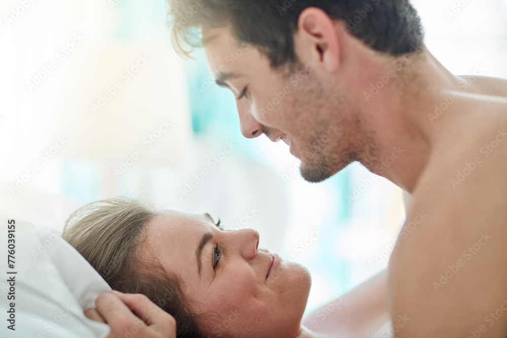 Fototapeta premium Happy, love and couple in bed with romance, intimacy and desire, connection and bonding in their home together. Foreplay, eye contact and people in a bedroom with passion for honeymoon or anniversary