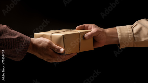 A mans hand passing a brown cardboard box to another persons hand on a black background photo