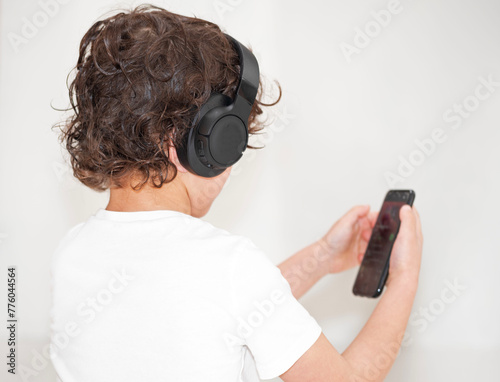 A young boy with headphones and a mobile phone in hand