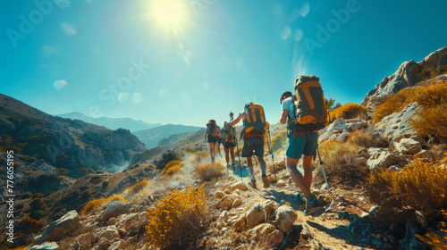 Hikers with gear walking through a dry mountain landscape with golden flora, illuminated by sunset.