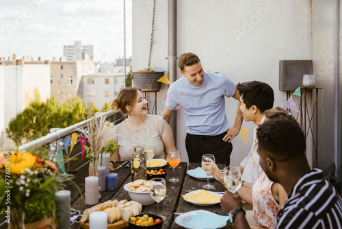 Happy male and female friends talking to each other while celebrating during dinner party in balcony photo