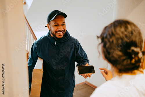 Happy male delivery person giving smart phone to woman for digital signature at doorstep photo
