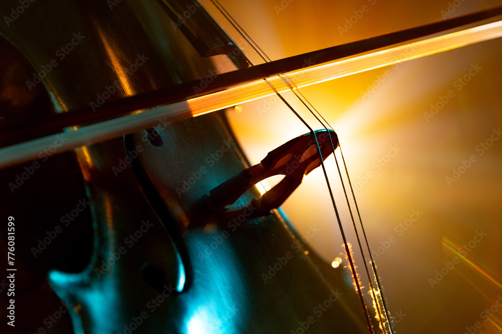 Detailed photo of classical cello with bow in golden-yellow stage light casting vibrant shadows. Solo performance. Concept of hobby and work, music festivals, concerts, symphony show, culture.