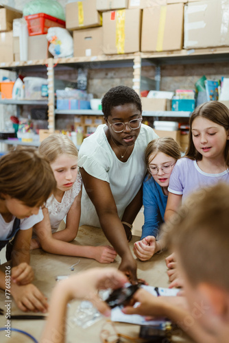 Female teacher assisting group of students working on robotics project at workshop photo