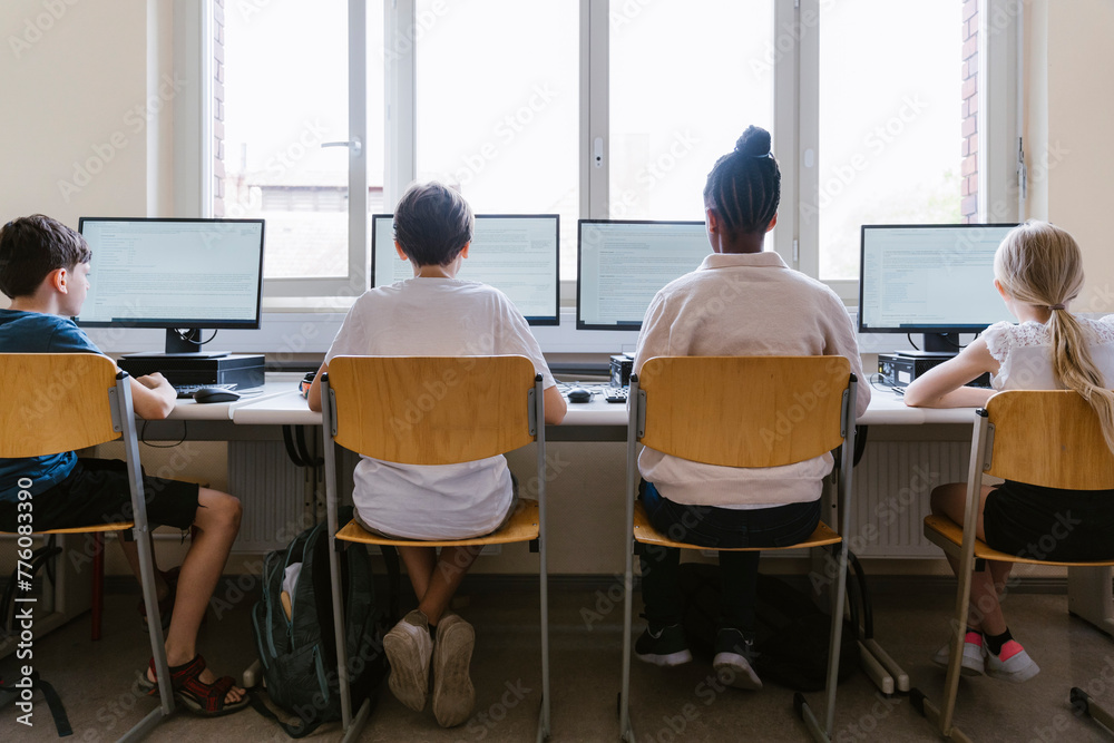 Rear view of male and female students using computers while sitting in classroom at school Rear view of male and female students using computers while sitting in classroom at school