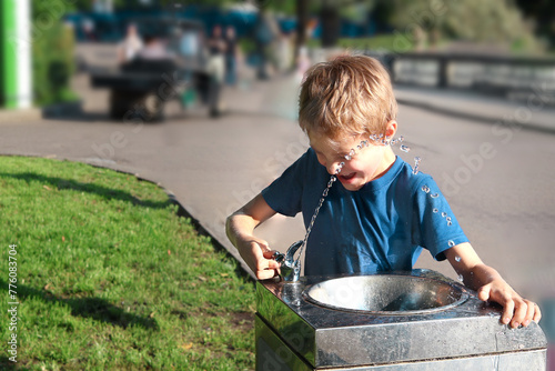 Quadro em tela 7-year-old boy in summer park tries to drink water from street drinking fountain, he fails, and stream with large drops flies past